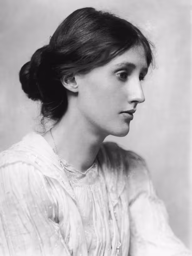 A black and white portrait photograph of a young woman, likely Virginia Woolf, shown in profile looking to the right. She has dark hair styled in an updo or low bun. She is wearing a light-colored, high-collared blouse with a textured or ruffled fabric. The image is cropped vertically and displayed centered against a black background on a computer screen.