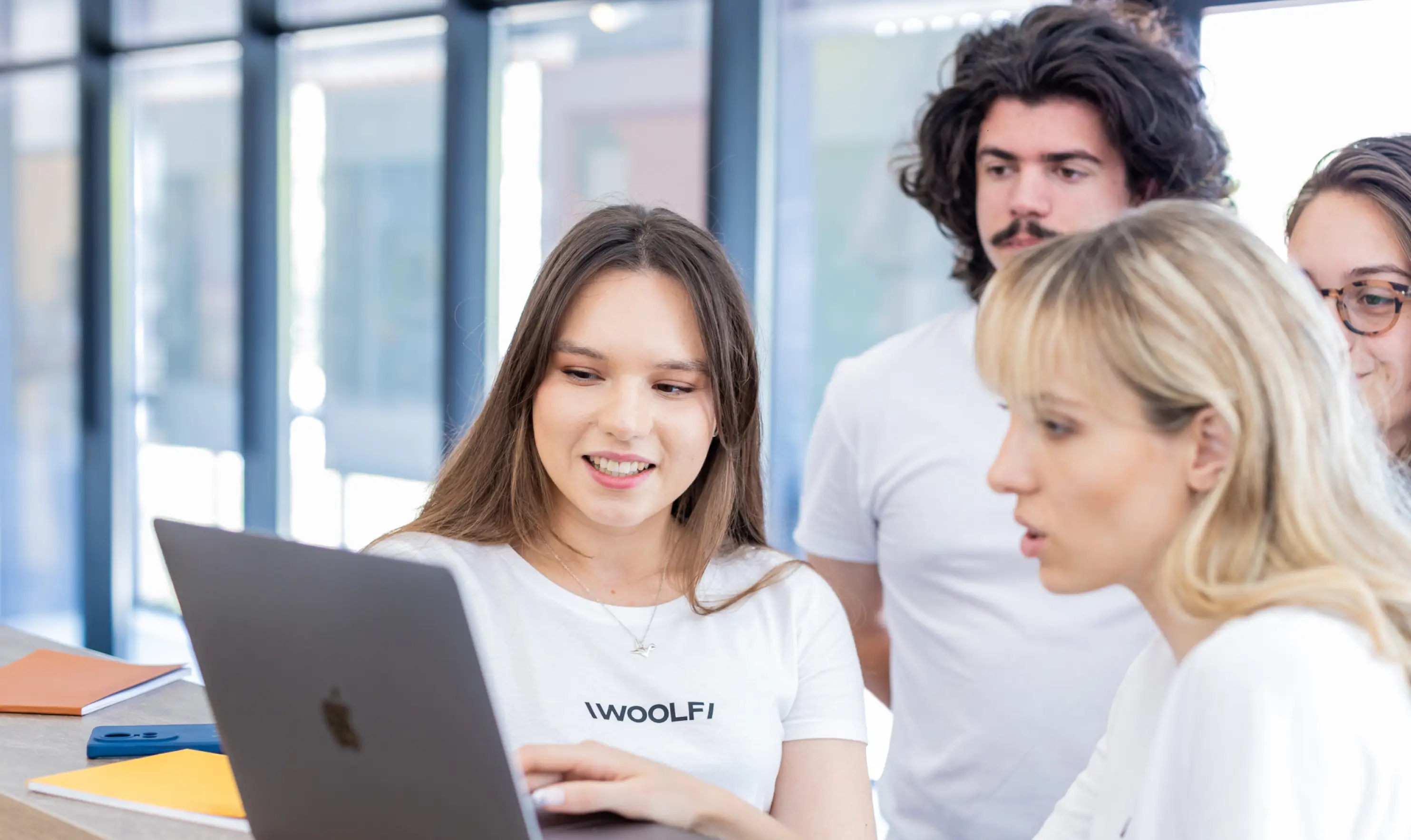 Four young adults collaborating around a MacBook laptop
